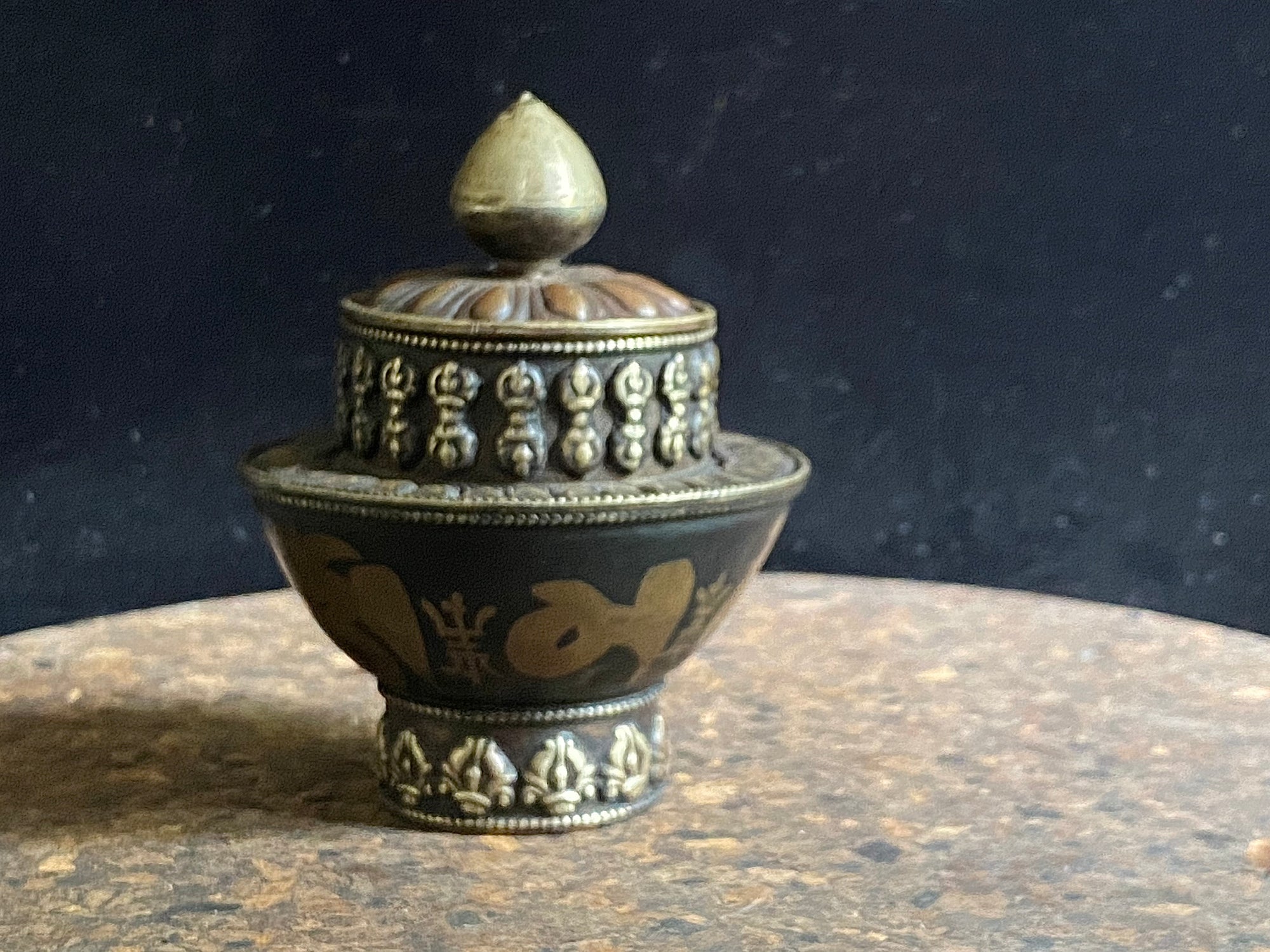 Brass, copper and white metal shaped pot with lid - incense burner, offering bowl or trinket bowl. Topped with a representation of a lotus bud, ringed with dorjes, the mantra Om Mani Padme Hum  and a border of Golden Fish (one of the Eight Auspicious Symbols representing good fortune). Height 11 cm x 8 cm