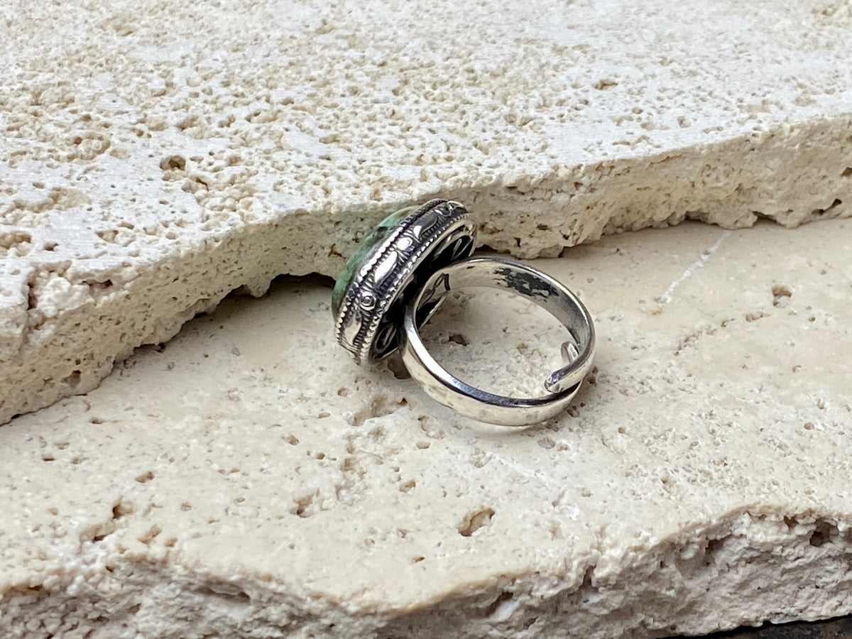 This simple ring features a large antique cabochon turquoise stone, set in a simple patterned silver bezel, with an adjustable ring band. As is the case with many of the rings we are currently buying, the stone is old and has been reset into a new silver band.  Measurements:  Ring face 2 x 1.5 cm Inner diameter 16.5 mm | Size 6 , however the adjustable band will fit any finger sized 5 -7