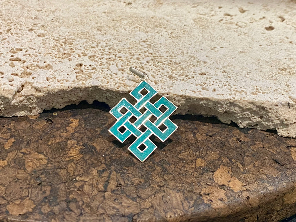 Sterling silver and turquoise Endless Knot pendant, one of the eight auspicious symbols of Buddhism. Sterling silver, set with ground chips of turquoise in enamel, from Nepal. Height 4 cm including bail