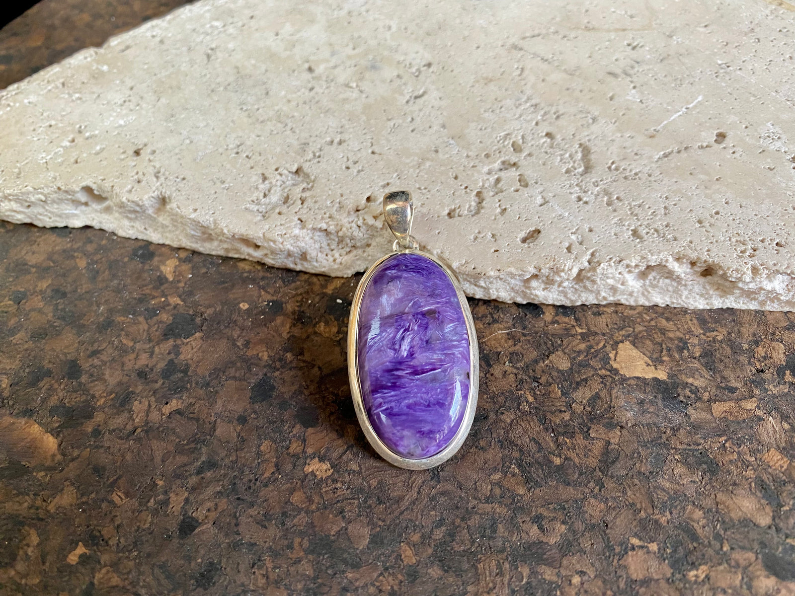 This lustrous charoite pendant is set off by a sterling silver bezel, topped by a bail that’s large enough to accommodate a thick chain or cord. A stunning piece of purple charoite with deep colour.  Measurements: 5.2 cm (2 in) height including bail, 2.2 cm (0.75 in) at widest point 