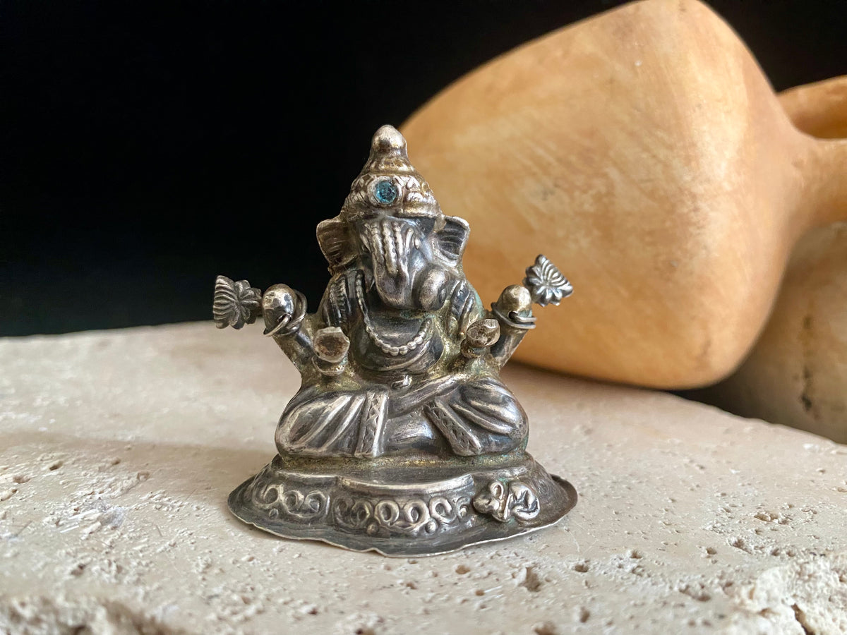 Small vintage Ganesh statue cast in silver, with right hand up in the gesture of protection and left hand holding his favourite ladoo sweet. His other hands hold lotus flowers. Lightweight but very finely cast with a small facet cut blue topaz in his forehead. 50 years old, southern India. 5 cm height