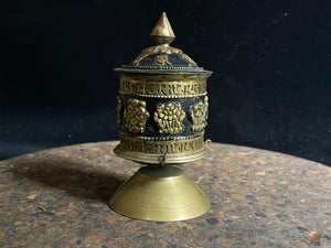 Standing prayer wheel, copper and brass, weighted for spinning and containing a scroll on which is printed the mantra "Om Mani Padme Hum", a prayer to the Compassionate Buddha, printed many times over. Measurements: height 12 cm, diameter 6.3 cm