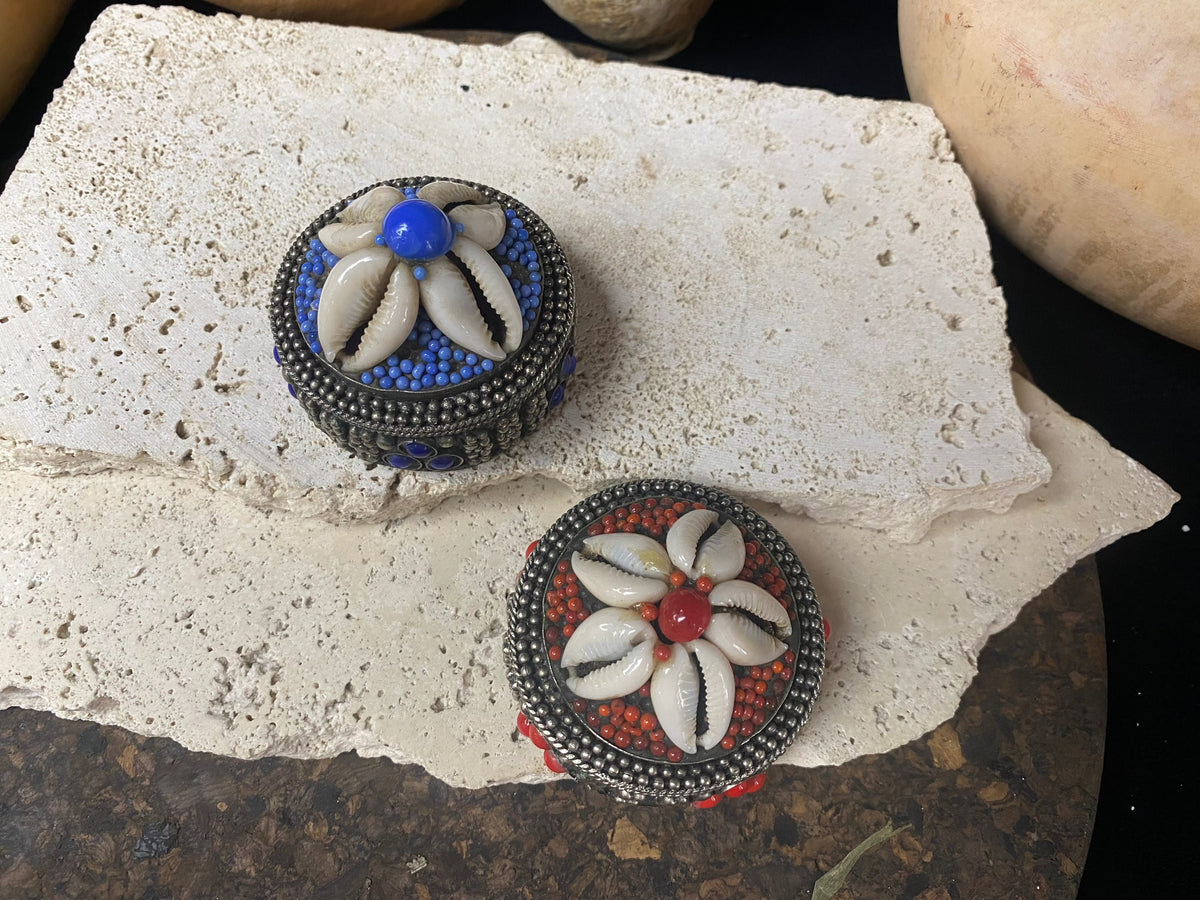 Small round pill or trinket boxes. Metal with bead and cowrie shell decoration. Tight fitting lid. Velvet lined, including inside the lid. These are perfect trinket boxes for kids, and would also make a very nice jewellery presentation box for gifting jewellery.  Measurements: 5.5 cm (2.25") diameter, height 5 cm (2")   