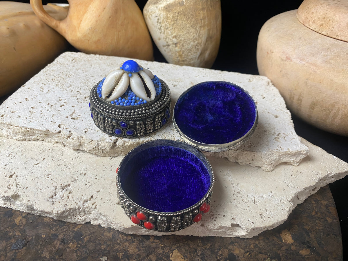 Small round pill or trinket boxes. Metal with bead and cowrie shell decoration. Tight fitting lid. Velvet lined, including inside the lid. These are perfect trinket boxes for kids, and would also make a very nice jewellery presentation box for gifting jewellery.  Measurements: 5.5 cm (2.25") diameter, height 5 cm (2")   