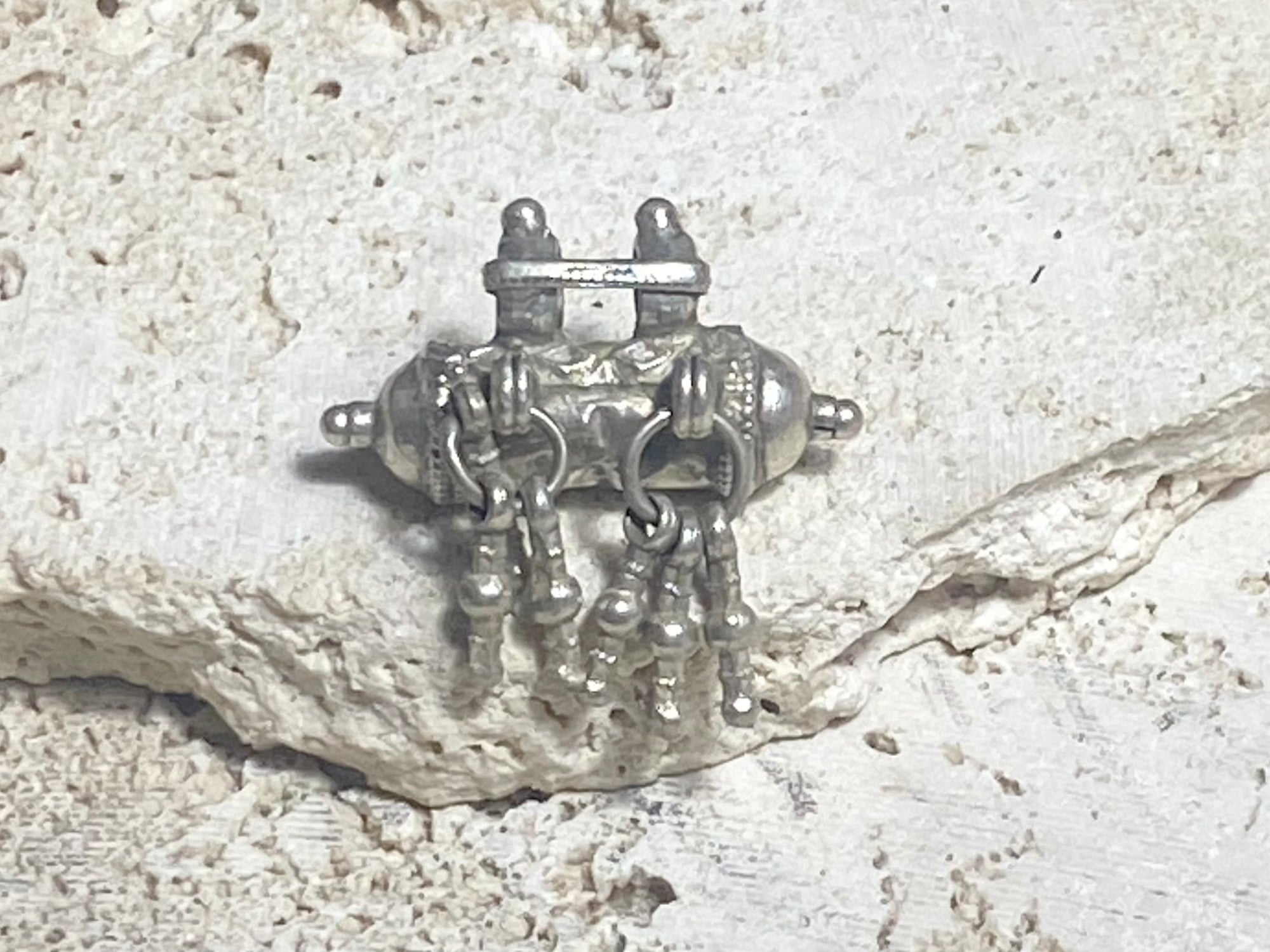 High grade silver amulet with fused ends, early 20th century, from northern India. The decoration is unusual, with a bar connecting the bails and a set of silver dangles fused together. Measurements: length 3.1 cm, diameter 1.5 cm, height including dangles 3 cm