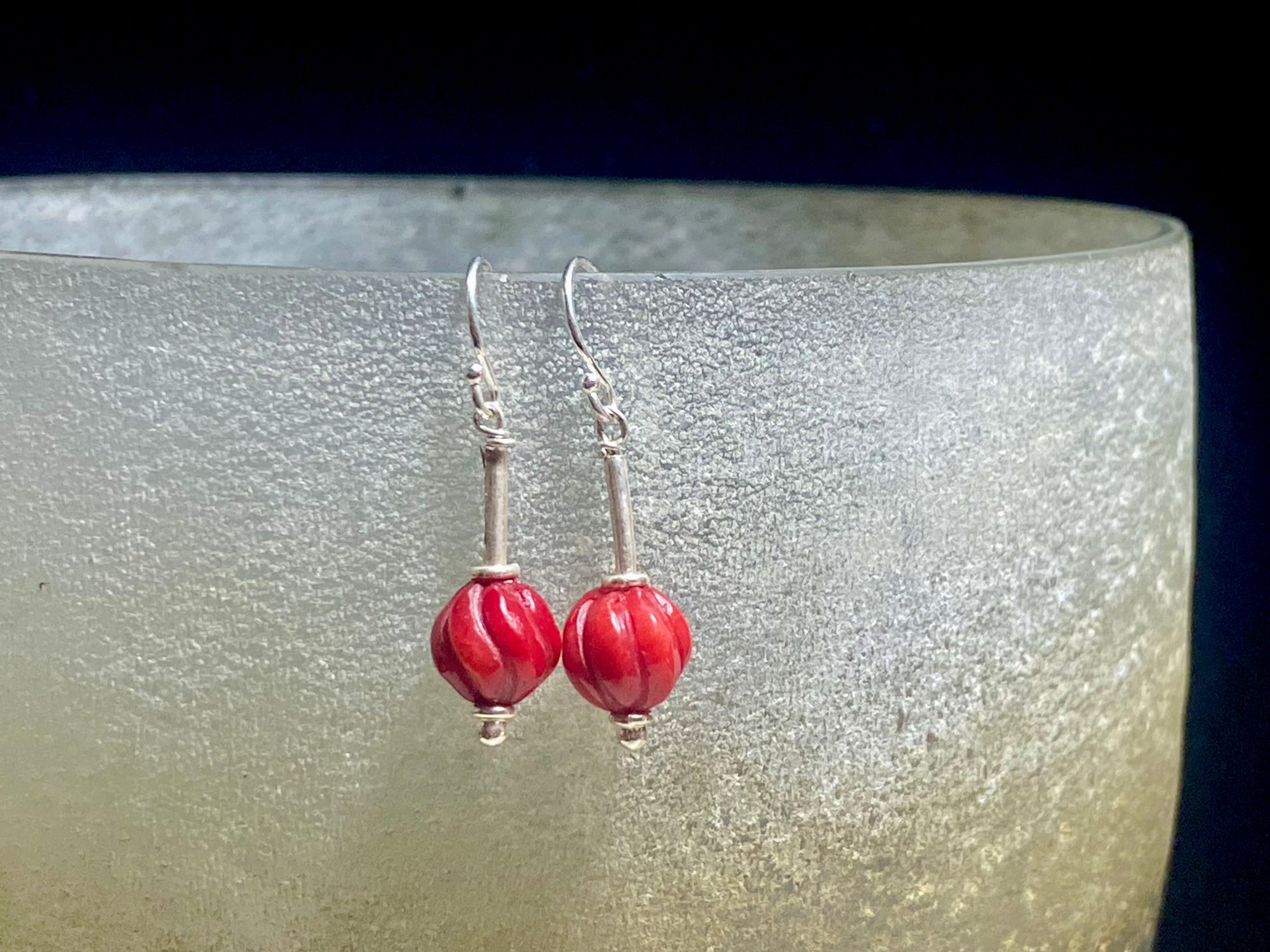 A simple earring featuring a hand carved red coral bead and sterling silver handmade Indian beads with silver hooks. Light and easy to wear, and a petite, classic earring. Measurements: 3 cm length including hook