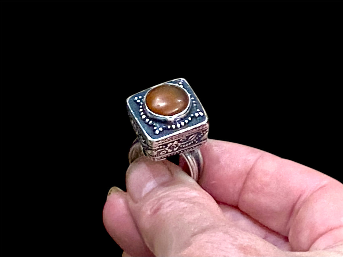 An unusual ring featuring a round carnelian stone set in a high box setting. Afghanistan, mid to late 20th century. Can be worn by either men or women. Measurements: Ring face 2.5 x 2.5, cm, height 1.5 cm. This is an adjustable ring spanning sizes 7 - 8