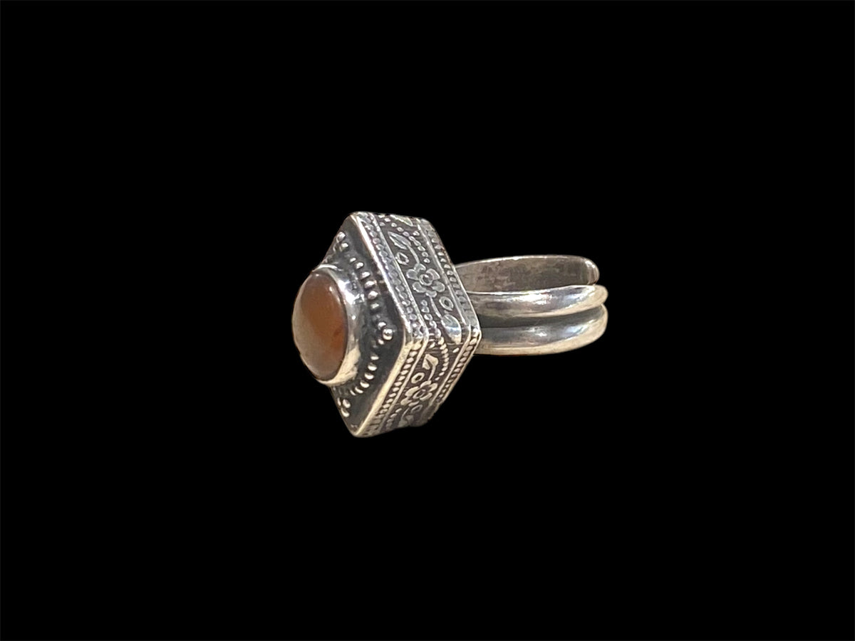 An unusual ring featuring a round carnelian stone set in a high box setting. Afghanistan, mid to late 20th century. Can be worn by either men or women. Measurements: Ring face 2.5 x 2.5, cm, height 1.5 cm. This is an adjustable ring spanning sizes 7 - 8
