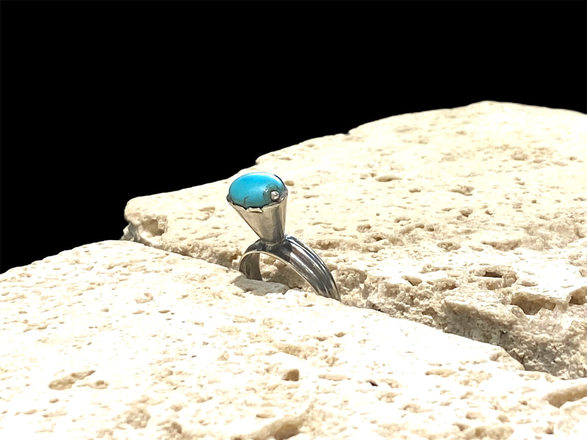 This unusual ring features an oval turquoise stone, set in a very high conical mount over a slender band. The turquoise stone is of excellent quality and contains very little matrix. Central Asia. Circa 1930. Stone 1 x 0.8 cm. Size 7 | 17.5 mm