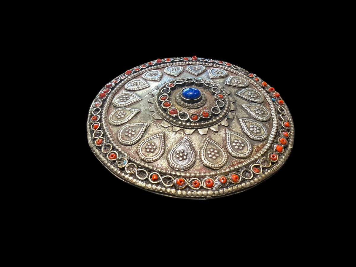 Turkoman pectoral pendant  (selpi guljaka). Applied leaf motifs, granulation and wire work set with ceramic beads (some of which are missing) and a central lapis cabochon. High grade silver. At the back is a soldered flat loop for attachment to the garment. Late 19th century. Diameter 9.5 cm