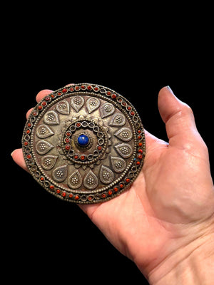 Turkoman pectoral pendant  (selpi guljaka). Applied leaf motifs, granulation and wire work set with ceramic beads (some of which are missing) and a central lapis cabochon. High grade silver. At the back is a soldered flat loop for attachment to the garment. Late 19th century. Diameter 9.5 cm