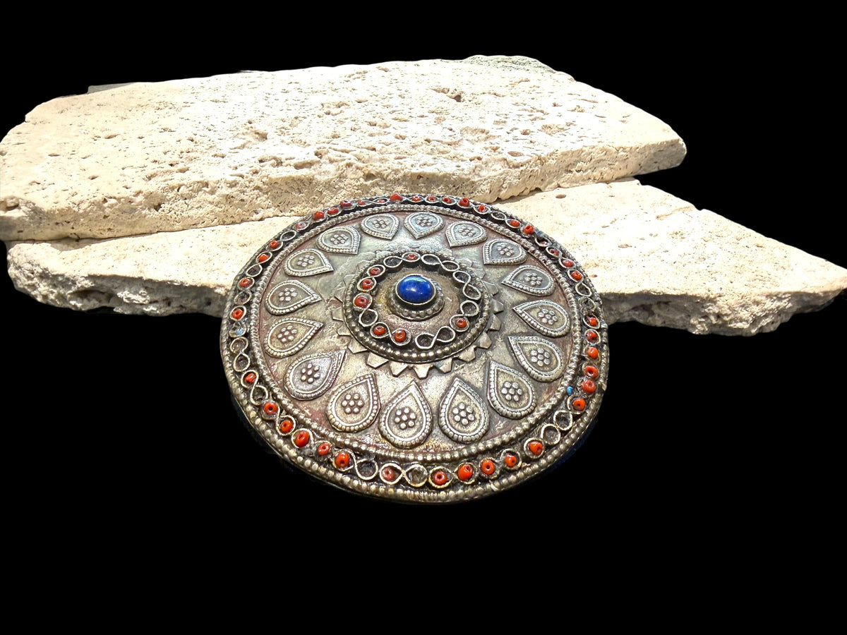 Turkoman pectoral pendant  (selpi guljaka). Applied leaf motifs, granulation and wire work set with ceramic beads (some of which are missing) and a central lapis cabochon. High grade silver. At the back is a soldered flat loop for attachment to the garment. Late 19th century. Diameter 9.5 cm