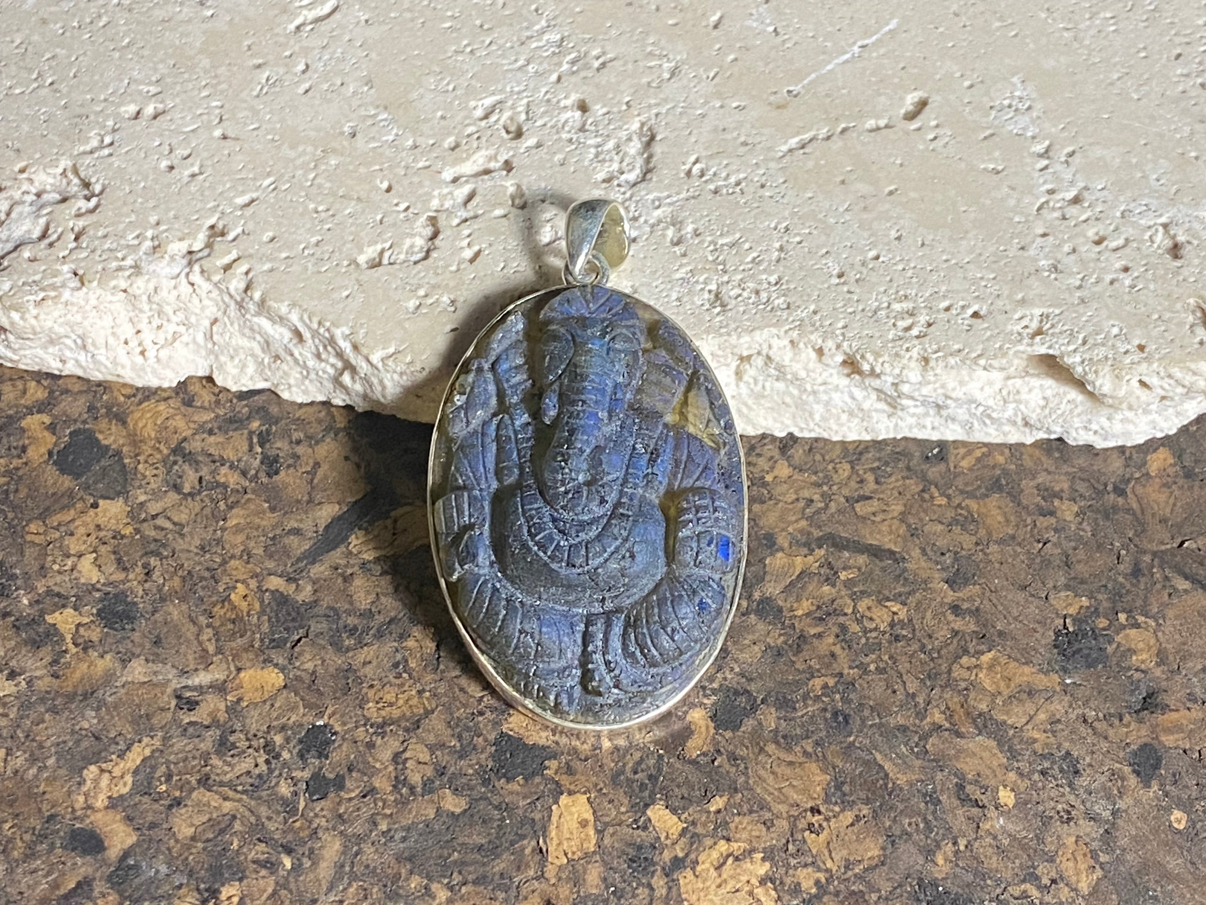 Hand carved labradorite pendant depicting Ganesh, elephant headed god of wisdom, prosperity and new beginnings. This is a unique and individual piece, with a luminosity enhanced by the depth of the stone, that changes depending on the angle of lighting. Sterling silver frame and bail. The bail is generous enough to allow a large chain or cord to pass through. This unisex labradorite pendant will suit both men and women. Measurements: height 5.5 cm including bail, width 3.1 cm