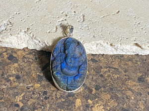 Hand carved labradorite pendant depicting Ganesh, elephant headed god of wisdom, prosperity and new beginnings. This is a unique piece, a medium/large oval pendant that has a very attractive deep blue luminosity that comes alive depending on the angle of lighting. Sterling silver frame and bail. The bail is generous enough to allow a large chain or cord to pass through.  This unisex labradorite pendant will suit both men and women.  Measurements: height 5.5 cm including bail, width 3 cm