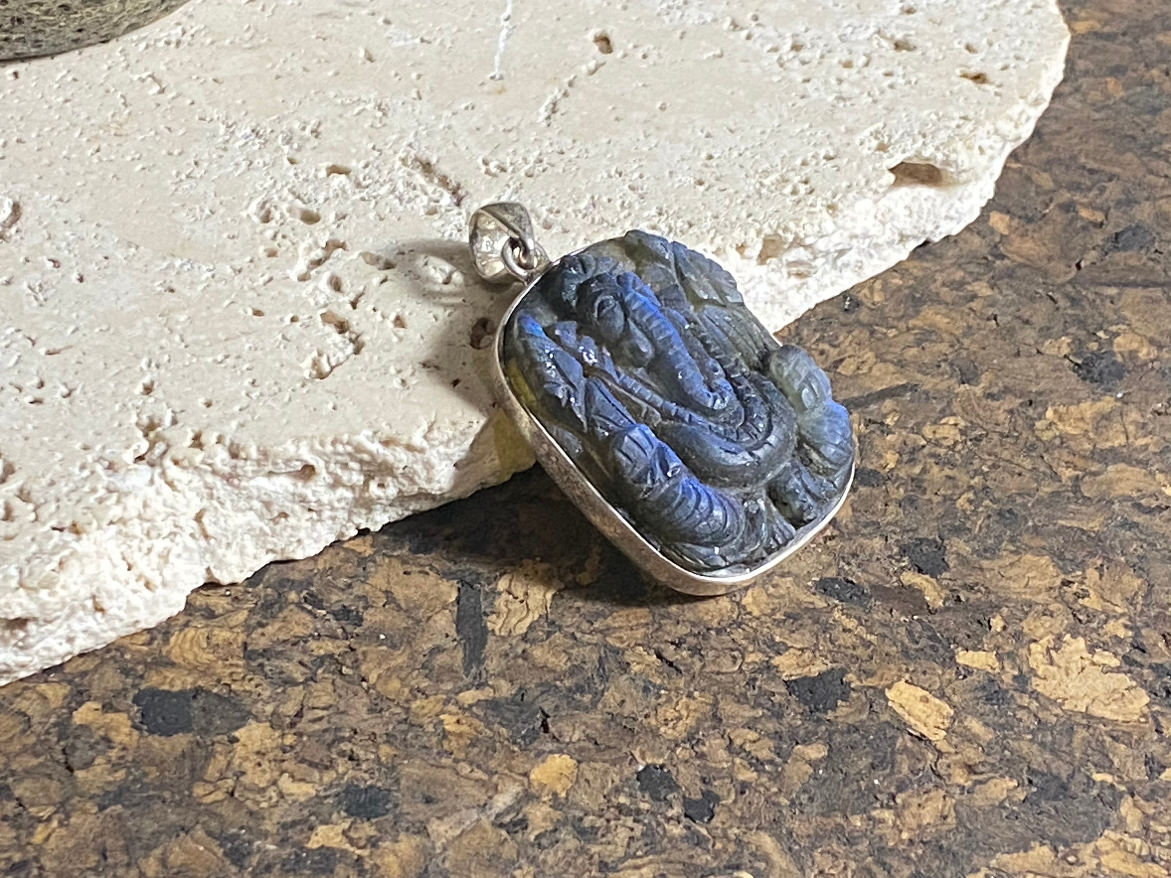 Hand carved square labradorite pendant depicting Ganesh, elephant headed god of wisdom, prosperity and new beginnings. This is a unique and individual piece, hand carved by an artisan in Jaipur, with a light blue luminosity that changes depending on the angle of lighting. Sterling silver frame and bail. The bail is generous enough to allow a large chain or cord to pass through. This unisex labradorite pendant will suit both men and women. Measurements: height 4.7 cm including bail, width 3 cm