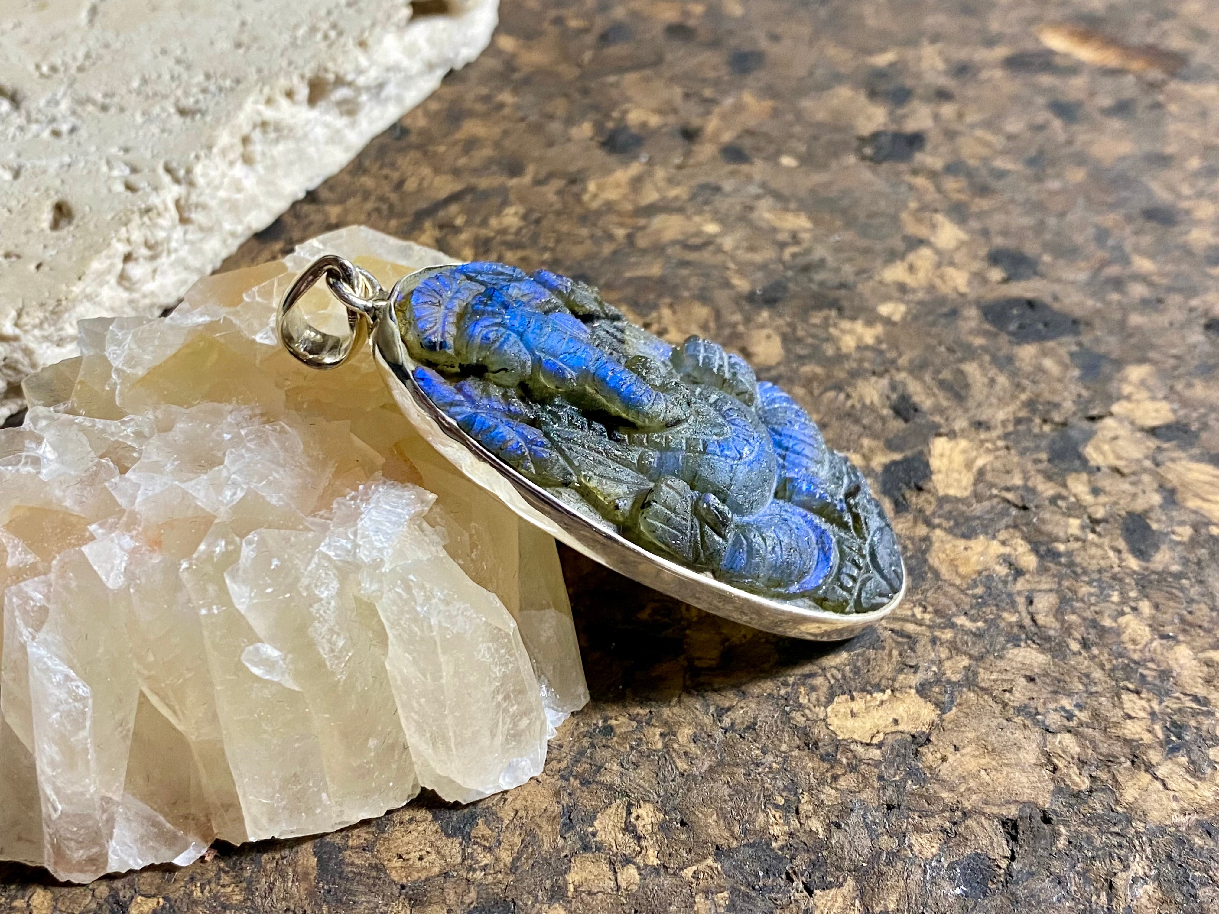 nd carved labradorite pendant depicting Ganesh, elephant headed god of wisdom, prosperity and new beginnings. This is a unique and individual piece, one of our largest, a long oval, with a dark luminosity that comes alive depending on the angle of lighting. Sterling silver frame and bail. The bail is generous enough to allow a large chain or cord to pass through. This unisex labradorite pendant will suit both men and women. Measurements: height 6.2 cm including bail, width 2.7 cm