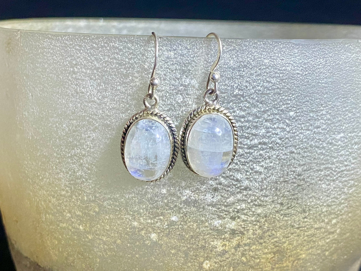Simple and elegant, these oval rainbow moonstone earrings feature cabochon cut rainbow moonstones and are finished with detailed sterling silver surrounds and very generous shepherd hooks. Measurements: height 3.2 mm (0.13 in) including hook, width 1.3 cm