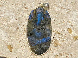 nd carved labradorite pendant depicting Ganesh, elephant headed god of wisdom, prosperity and new beginnings. This is a unique and individual piece, one of our largest, a long oval, with a dark luminosity that comes alive depending on the angle of lighting. Sterling silver frame and bail. The bail is generous enough to allow a large chain or cord to pass through.  This unisex labradorite pendant will suit both men and women.  Measurements: height 6.2 cm including bail, width 2.7 cm