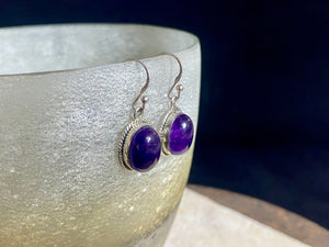 Amethyst earrings featuring high quality stones, classic darker cabochon amethysts with a detailed oval bezel. Sterling silver hook and mounts. Our amethyst earrings are open at the back to allow the natural light of the amethysts to shine through. Size 3.2 cm length including hook.