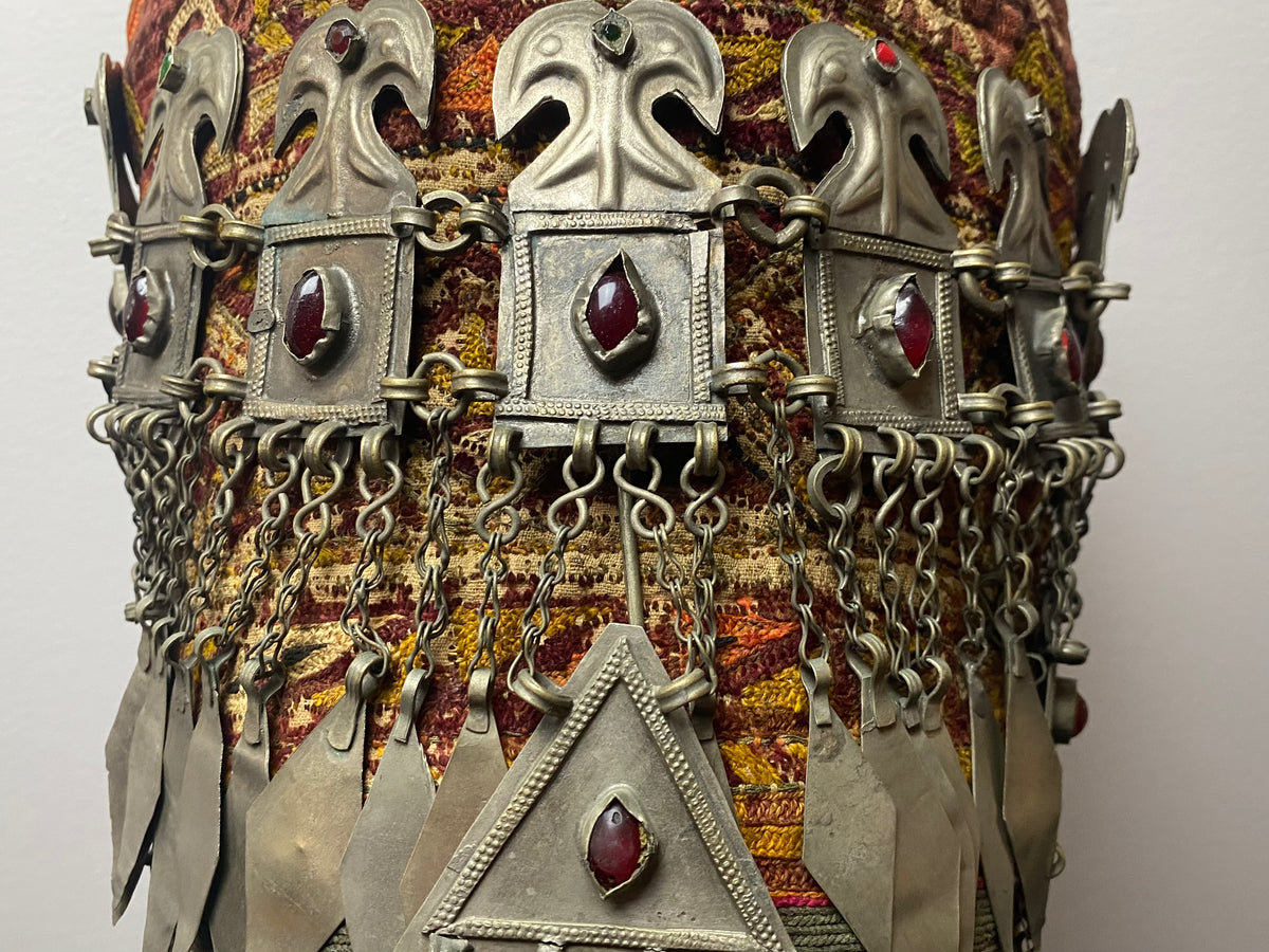 Ersari headdress consisting of a metal gaashbaagh & a high embroidered conical hat into which it attached with long spikes. The cap is quilted cotton covered in velvet and detailed silk embroidery. An heirloom piece, dating from 1870-1890. Cap height 23 cm. Tiara: width 53 cm, height of band 7 cm, side dangles 44 cm