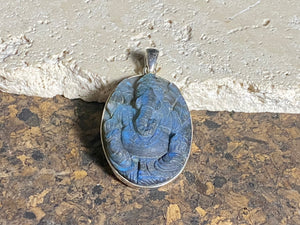 Hand carved labradorite pendant depicting Ganesh, elephant headed god of wisdom, prosperity and new beginnings. This is a unique and individual piece, with a deep blue luminosity enhanced by the depth of the stone, that changes depending on the angle of lighting. Sterling silver frame and bail. The bail is generous enough to allow a large chain or cord to pass through.  This unisex labradorite pendant will suit both men and women.  Measurements: height 5.2 cm including bail, width 3 cm