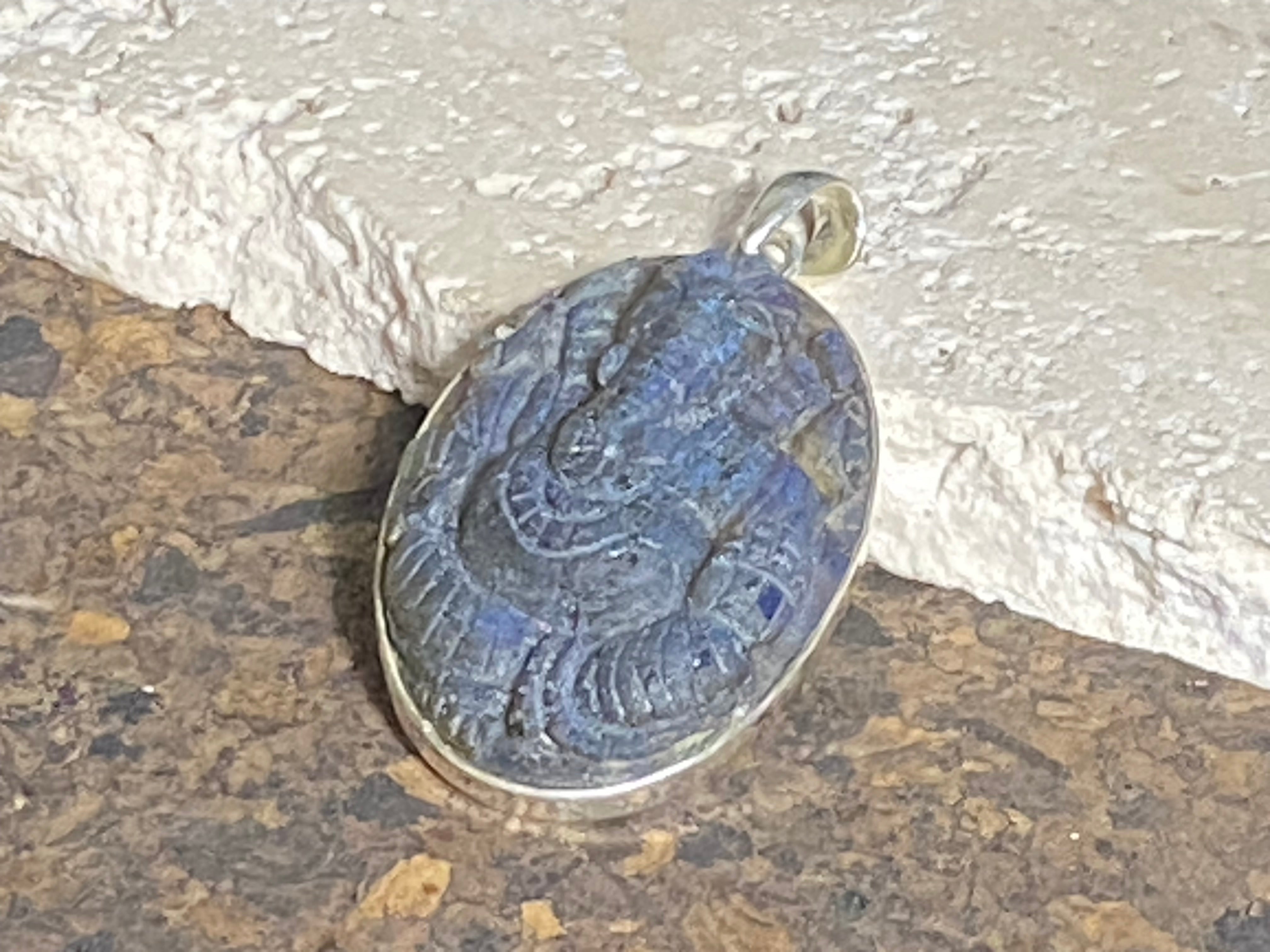 Hand carved labradorite pendant depicting Ganesh, elephant headed god of wisdom, prosperity and new beginnings. This is a unique and individual piece, with a luminosity enhanced by the depth of the stone, that changes depending on the angle of lighting. Sterling silver frame and bail. The bail is generous enough to allow a large chain or cord to pass through. This unisex labradorite pendant will suit both men and women. Measurements: height 5.5 cm including bail, width 3.1 cm