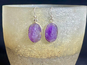 Hand carved from gem quality translucent amethyst and set in a silver surrounds and hooks, these unique earrings feature beautifully detailed images of the Hindu god Ganesh. Stunning and unique. Measurements: Drop including hooks 4 cm, width 1.5 cm