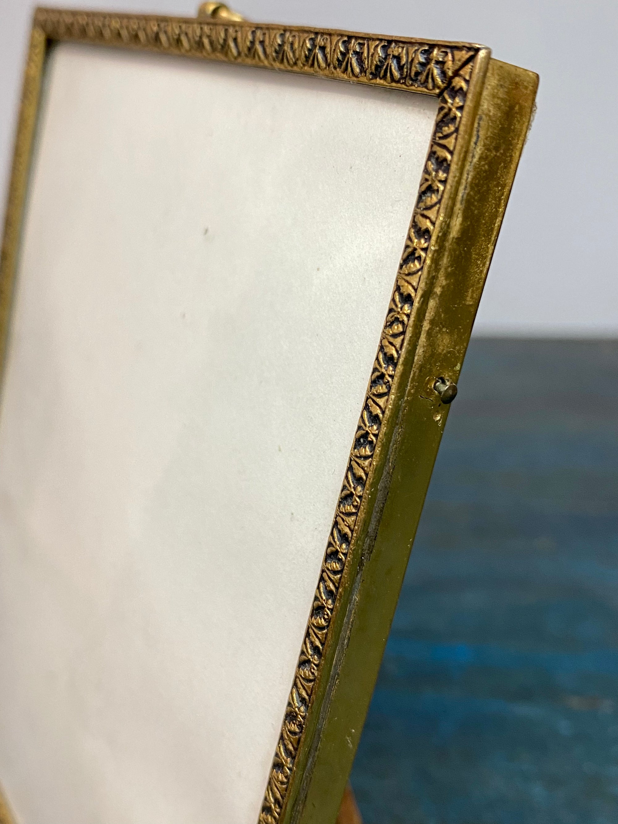This charming old frame appears to be gilt over brass, with a repeating border, ring at the top and a stand. The original back is covered in brown velvet and fits into the frame via side pins. Our vintage frame shows wear but is in good condition. Circa 1930, England. Outside frame 12.3 x 9.5 cm, inside 11.2 x 8.7 cm.