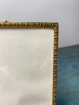 This charming old frame appears to be gilt over brass, with a repeating border, ring at the top and a stand. The original back is covered in brown velvet and fits into the frame via side pins. Our vintage frame shows wear but is in good condition. Circa 1930, England. Outside frame 12.3 x 9.5 cm, inside 11.2 x 8.7 cm.