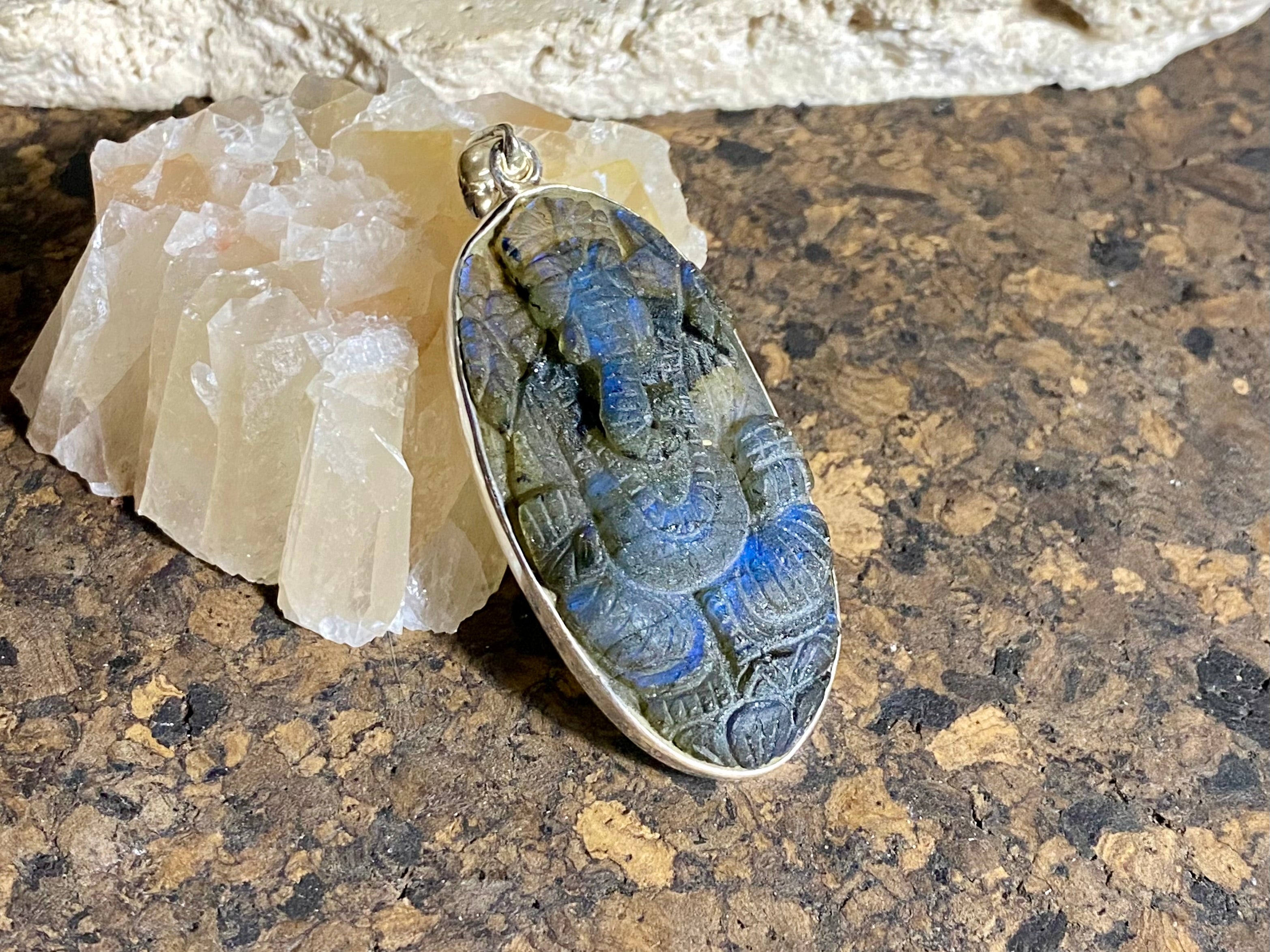 nd carved labradorite pendant depicting Ganesh, elephant headed god of wisdom, prosperity and new beginnings. This is a unique and individual piece, one of our largest, a long oval, with a dark luminosity that comes alive depending on the angle of lighting. Sterling silver frame and bail. The bail is generous enough to allow a large chain or cord to pass through. This unisex labradorite pendant will suit both men and women. Measurements: height 6.2 cm including bail, width 2.7 cm