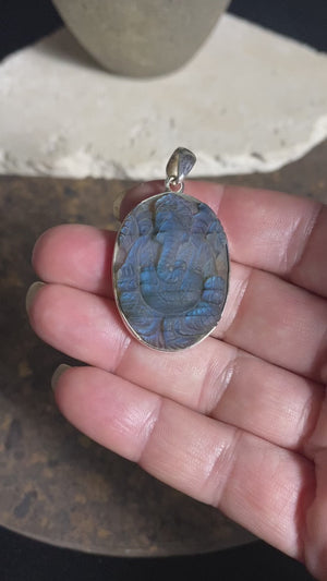 Hand carved labradorite pendant depicting Ganesh, elephant headed god of wisdom, prosperity and new beginnings. This is a unique piece, a smaller oval pendant that has a very attractive deep blue luminosity that comes alive depending on the angle of lighting. Sterling silver frame and bail. The bail is generous enough to allow a large chain or cord to pass through.  This unisex labradorite pendant will suit both men and women.  Measurements: height 4.6 cm including bail, width 2.7 cm