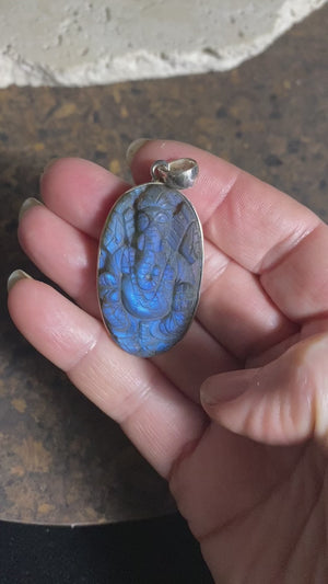 Hand carved labradorite pendant depicting Ganesh, elephant headed god of wisdom, prosperity and new beginnings. This is a unique and individual piece, a medium/large oval pendant that has a very attractive deep blue luminosity that comes alive depending on the angle of lighting. Sterling silver frame and bail. The bail is generous enough to allow a large chain or cord to pass through.  This unisex labradorite pendant will suit both men and women.  Measurements: height 5.3 cm including bail, width 2.6 cm