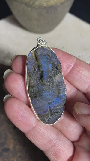 nd carved labradorite pendant depicting Ganesh, elephant headed god of wisdom, prosperity and new beginnings. This is a unique and individual piece, one of our largest, a long oval, with a dark luminosity that comes alive depending on the angle of lighting. Sterling silver frame and bail. The bail is generous enough to allow a large chain or cord to pass through.  This unisex labradorite pendant will suit both men and women.  Measurements: height 6.2 cm including bail, width 2.7 cm