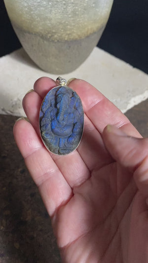 Hand carved labradorite pendant depicting Ganesh, elephant headed god of wisdom, prosperity and new beginnings. This is a unique piece, a medium/large oval pendant that has a very attractive deep blue luminosity that comes alive depending on the angle of lighting. Sterling silver frame and bail. The bail is generous enough to allow a large chain or cord to pass through.  This unisex labradorite pendant will suit both men and women.  Measurements: height 5.5 cm including bail, width 3 cm