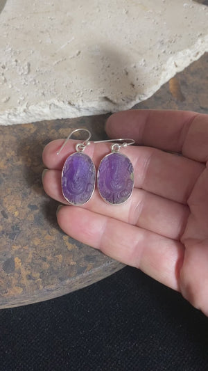 Hand carved from gem quality translucent amethyst and set in a silver surrounds and hooks, these unique earrings feature beautifully detailed images of the Hindu god Ganesh. Stunning and unique. Measurements: Drop including hooks 4 cm, width 1.5 cm