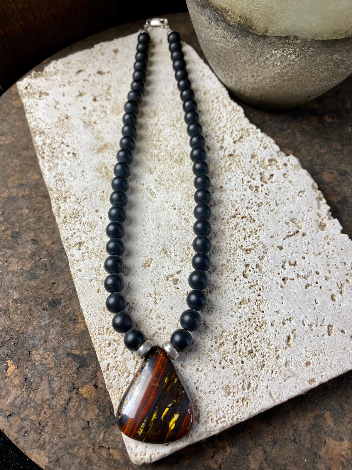 unique necklace of unpolished matte black onyx beads with a teardrop pendant of red tigers eye. Sterling silver clasp and detailing