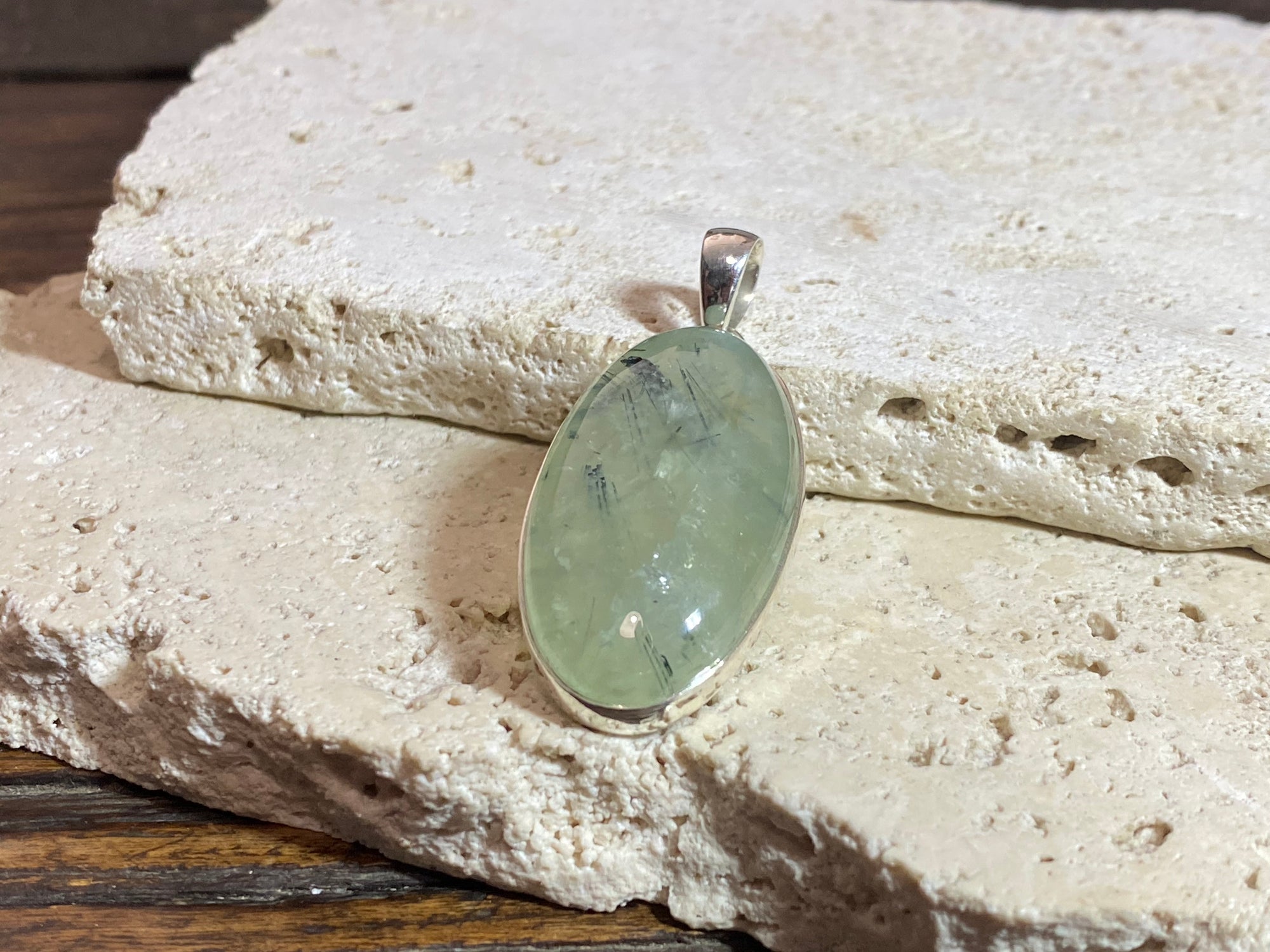 Large oval green prehnite with tourmaline inclusions set in a silver surround with a silver bail that is generous enough to take large chains or cords.