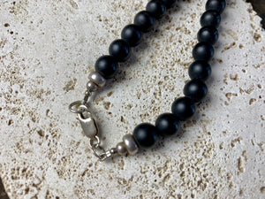 unique necklace of unpolished matte black onyx beads with a teardrop pendant of red tigers eye. Sterling silver clasp and detailing