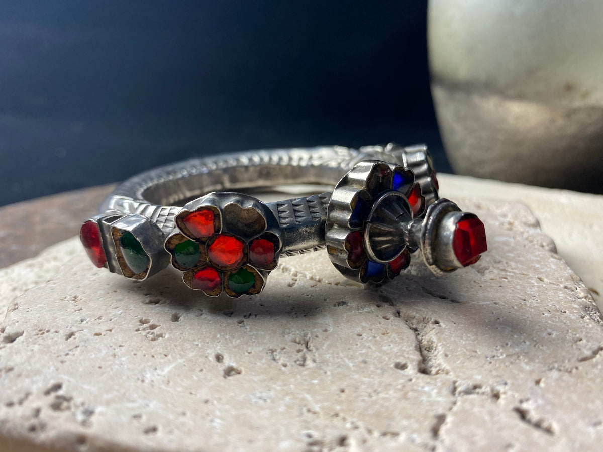 Very high grade silver, women's hinged cuff from Afghanistan. Hollow construction with a hexagon profile, this bracelet is hinged and features several florets of silver set with glass stones in red, blue and green, and a high profile reverse screw fastening and two stylised half opium poppies. 19th century