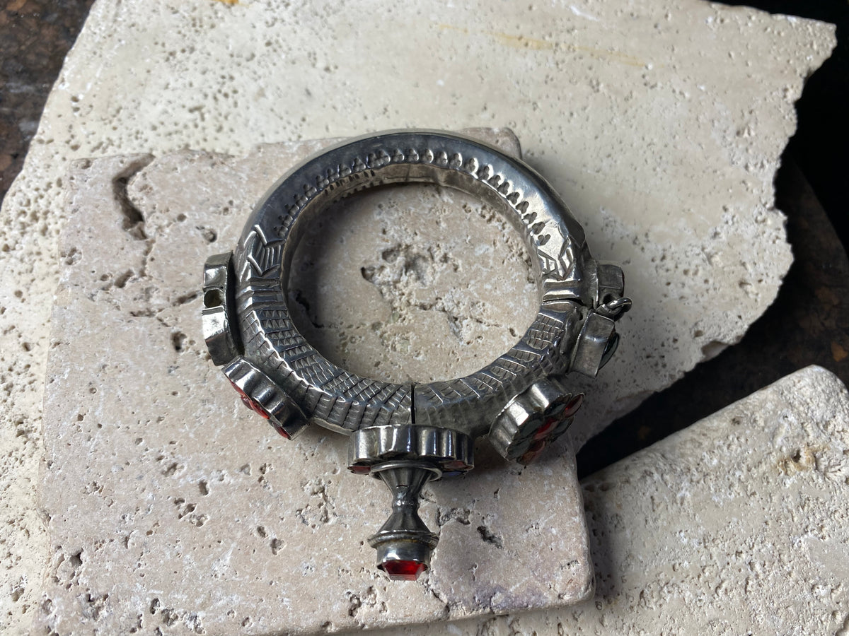 Very high grade silver, women's hinged cuff from Afghanistan. Hollow construction with a hexagon profile, this bracelet is hinged and features several florets of silver set with glass stones in red, blue and green, and a high profile reverse screw fastening and two stylised half opium poppies. 19th century