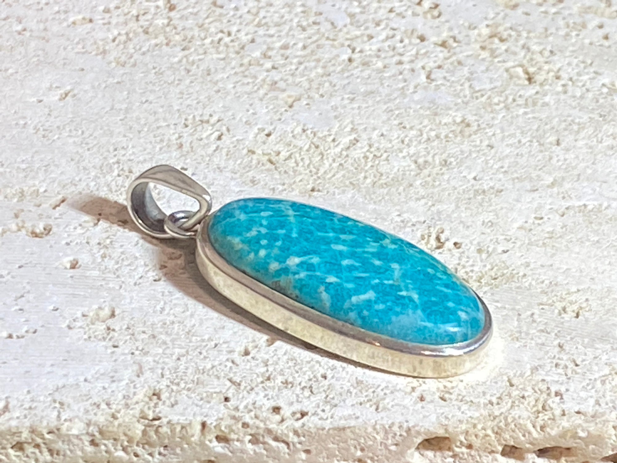 This unusual blue amazonite pendant is set off by a sterling silver bezel, topped by a bail that’s large enough to accommodate a thick chain or cord. A stunning piece of amazonite with a very unusual colour.