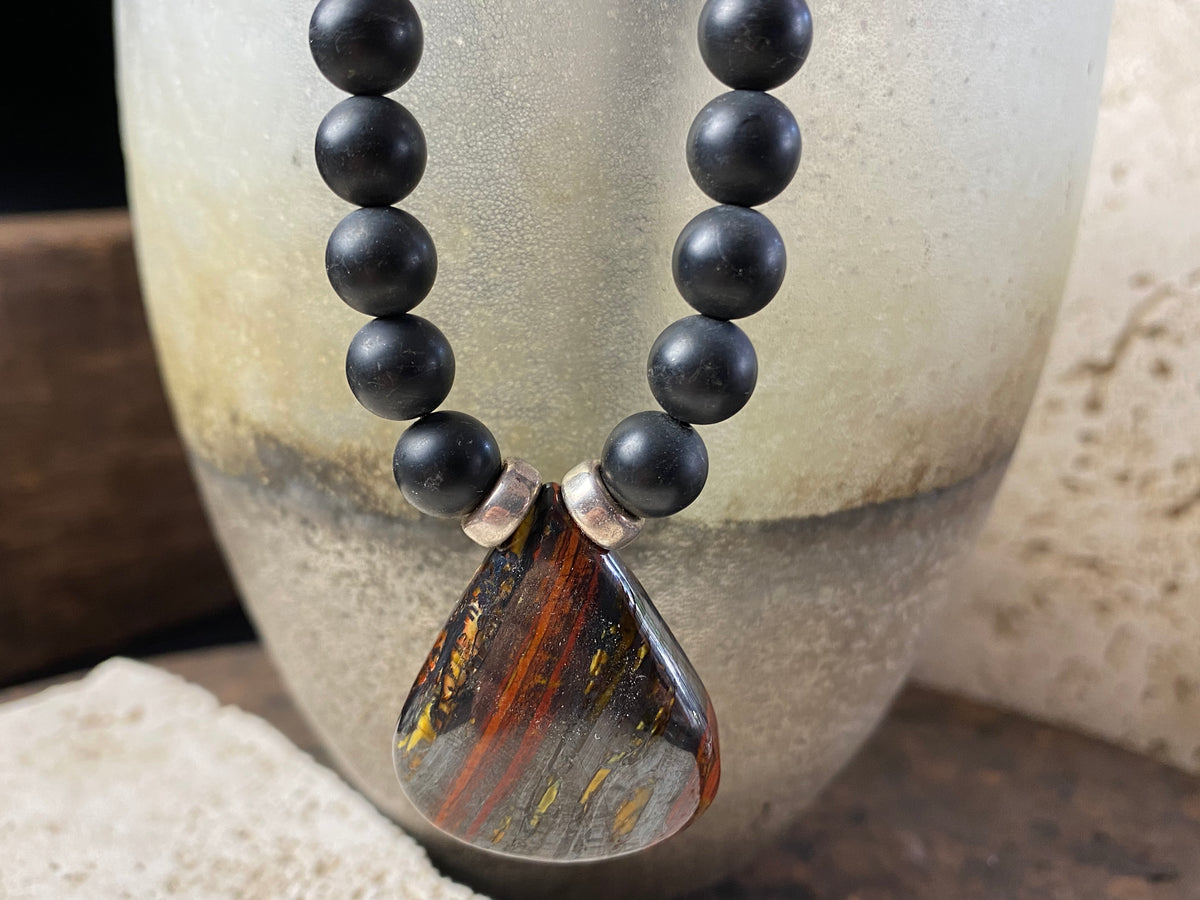 unique necklace of unpolished matte black onyx beads with a teardrop pendant of red tigers eye. Sterling silver clasp and detailing