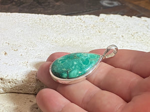 This strong green turquoise teardrop pendant is set off by a sterling silver bezel, topped by a bail that’s large enough to accommodate a thick chain or cord. Can be worn by men or women. A stunning piece of turquoise from Tibet. 