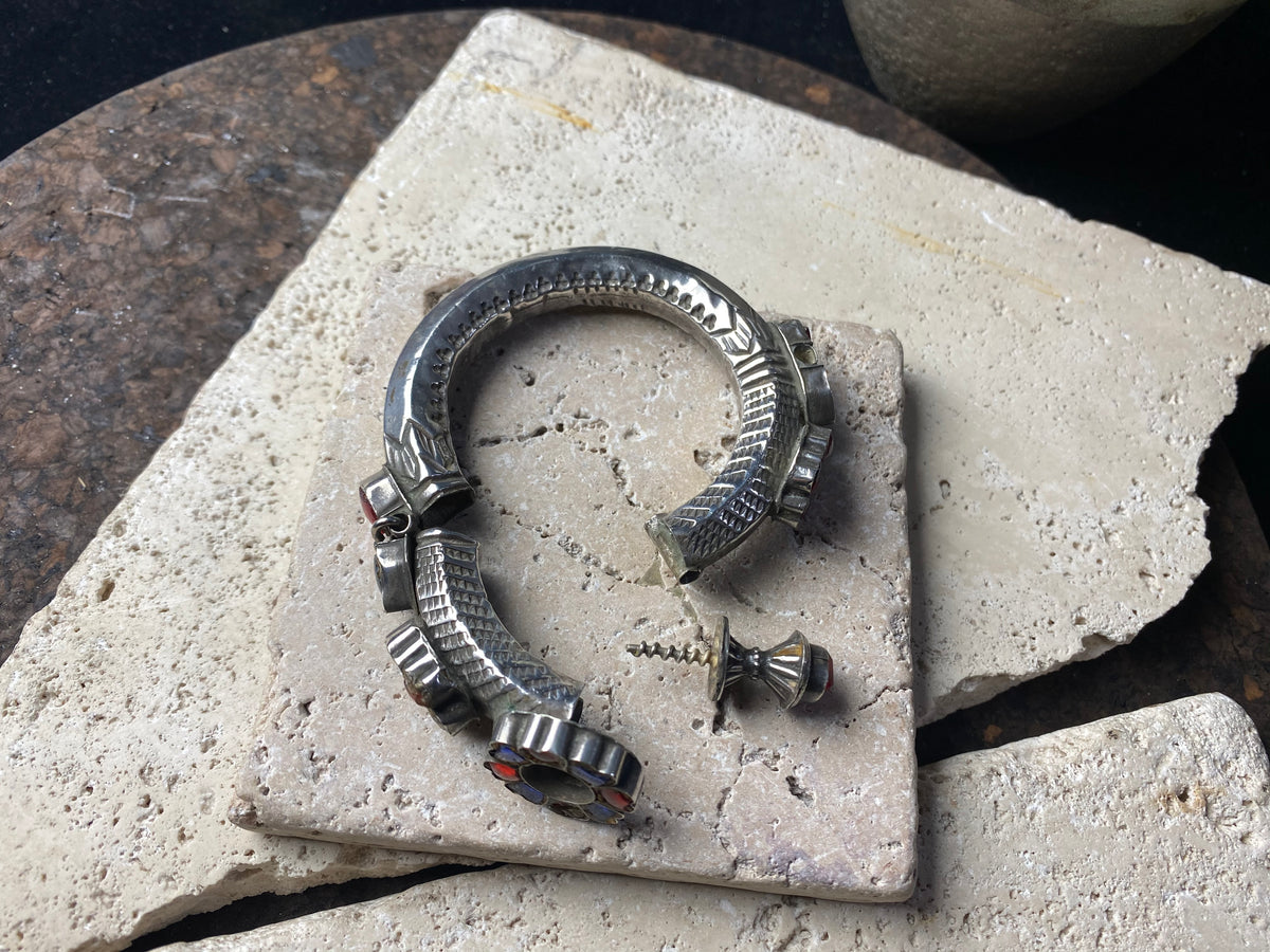 Very high grade silver, women's hinged cuff from Afghanistan. Hollow construction with a hexagon profile, this bracelet is hinged and features several florets of silver set with glass stones in red, blue and green, and a high profile reverse screw fastening and two stylised half opium poppies. 19th century