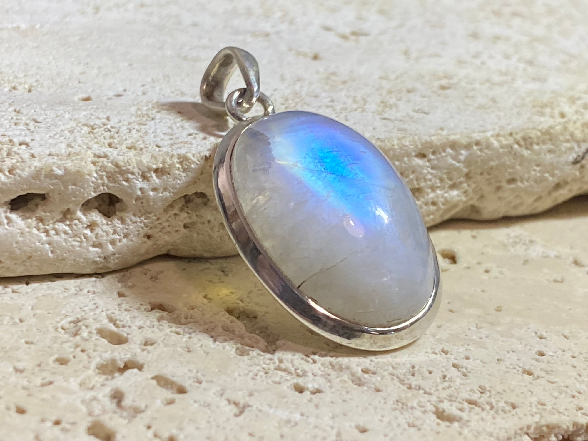 Oval high cut rainbow moonstone pendant set in sterling silver with a generous flexible bail to take a large chain or cord. A high quality stone with blue colour and fire. 