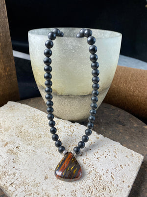 unique necklace of unpolished matte black onyx beads with a teardrop pendant of red tigers eye. Sterling silver clasp and detailing